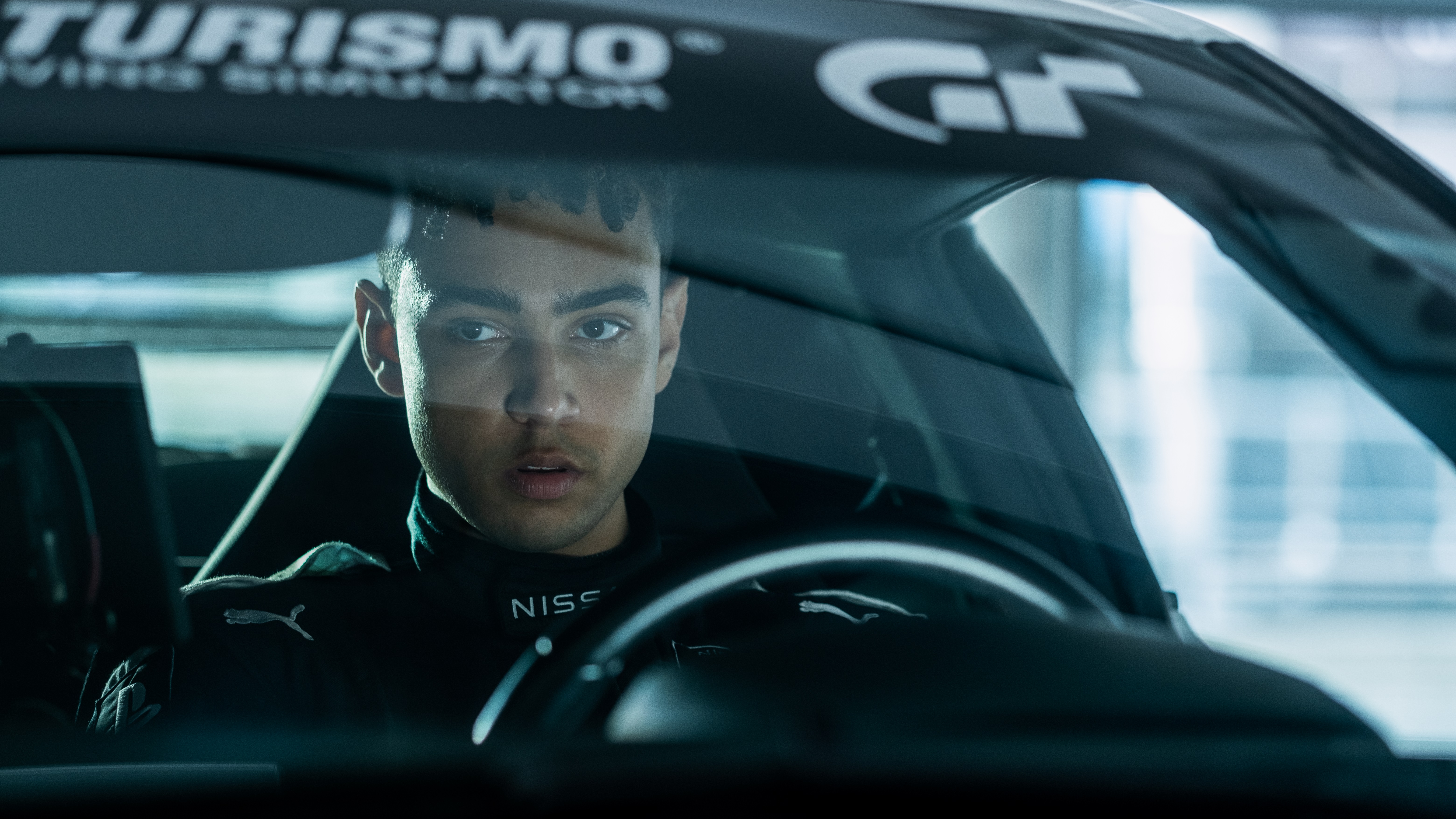 Archie Madekwe as Jann Mardenboroguh behind the wheel of a car with a Gran Turismo decal on the windscreen