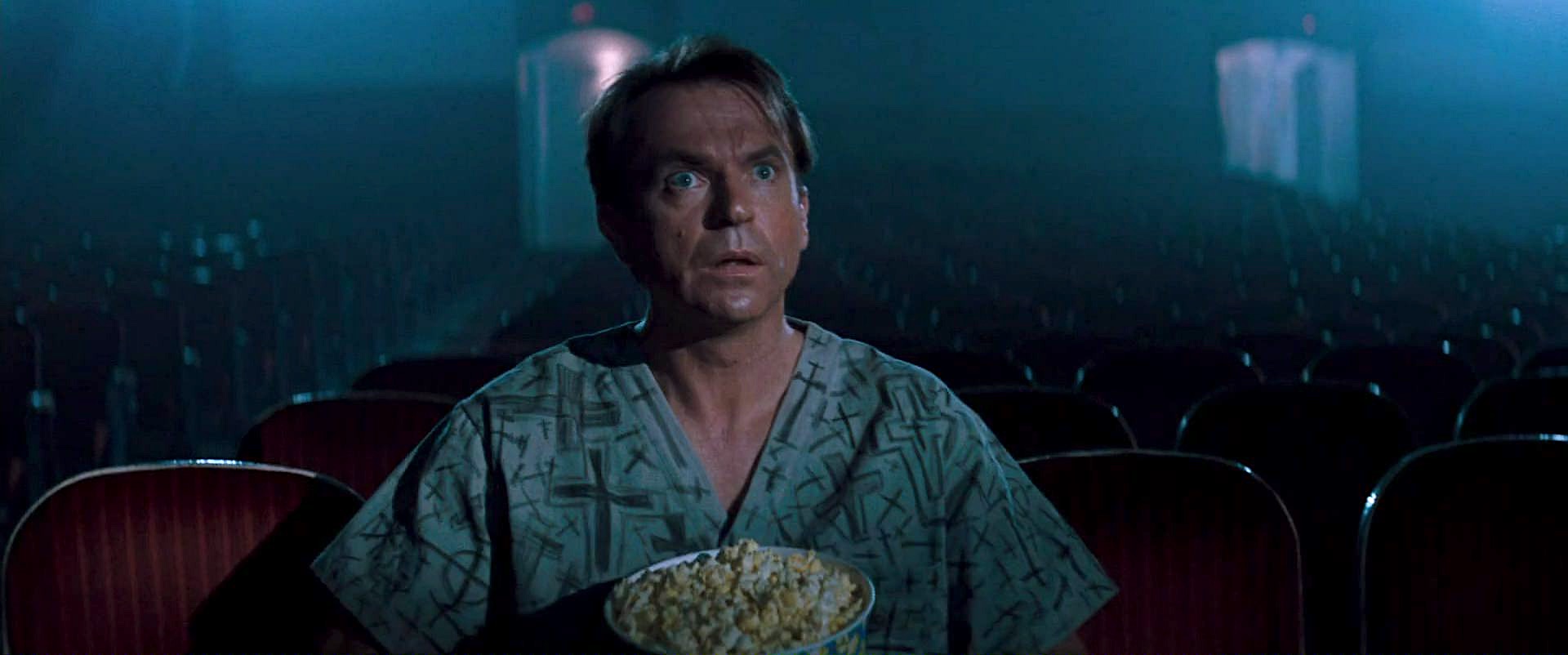 Sam Neill, sitting in a movie theater alone with a tub of popcorn, gapes at the screen in awe in the movie In the Mouth of Madness